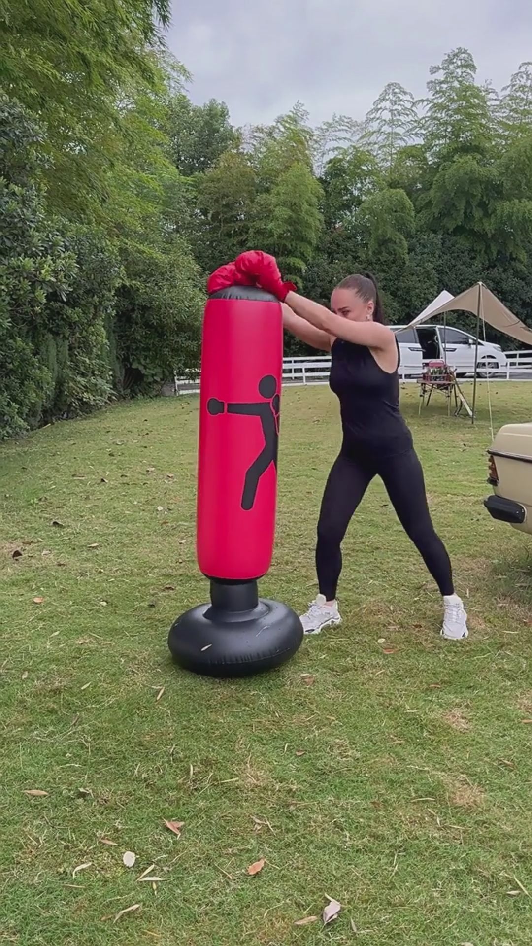 Load video: A young girl playing and punching a boxing column outside in the garden.